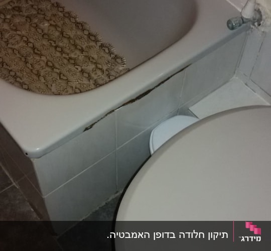 אמבטיה עם חיפוי פגום ליד אסלה
